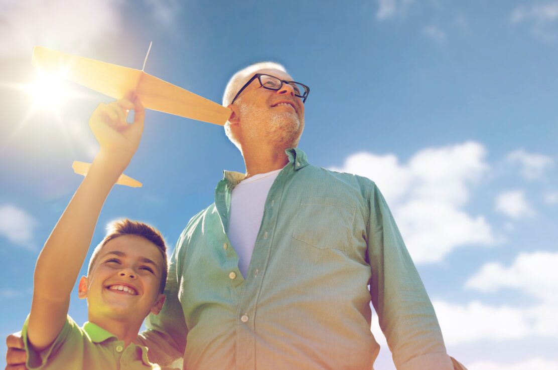 A grandfather and grandson playing with a toy plane outdoors.