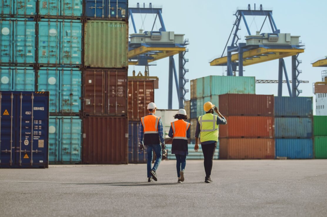 Workers walking through a shipping cargo container terminal depot.
