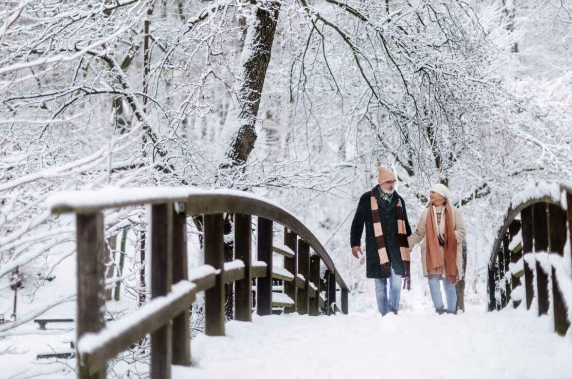 A couple walking across a bridge in the snow.